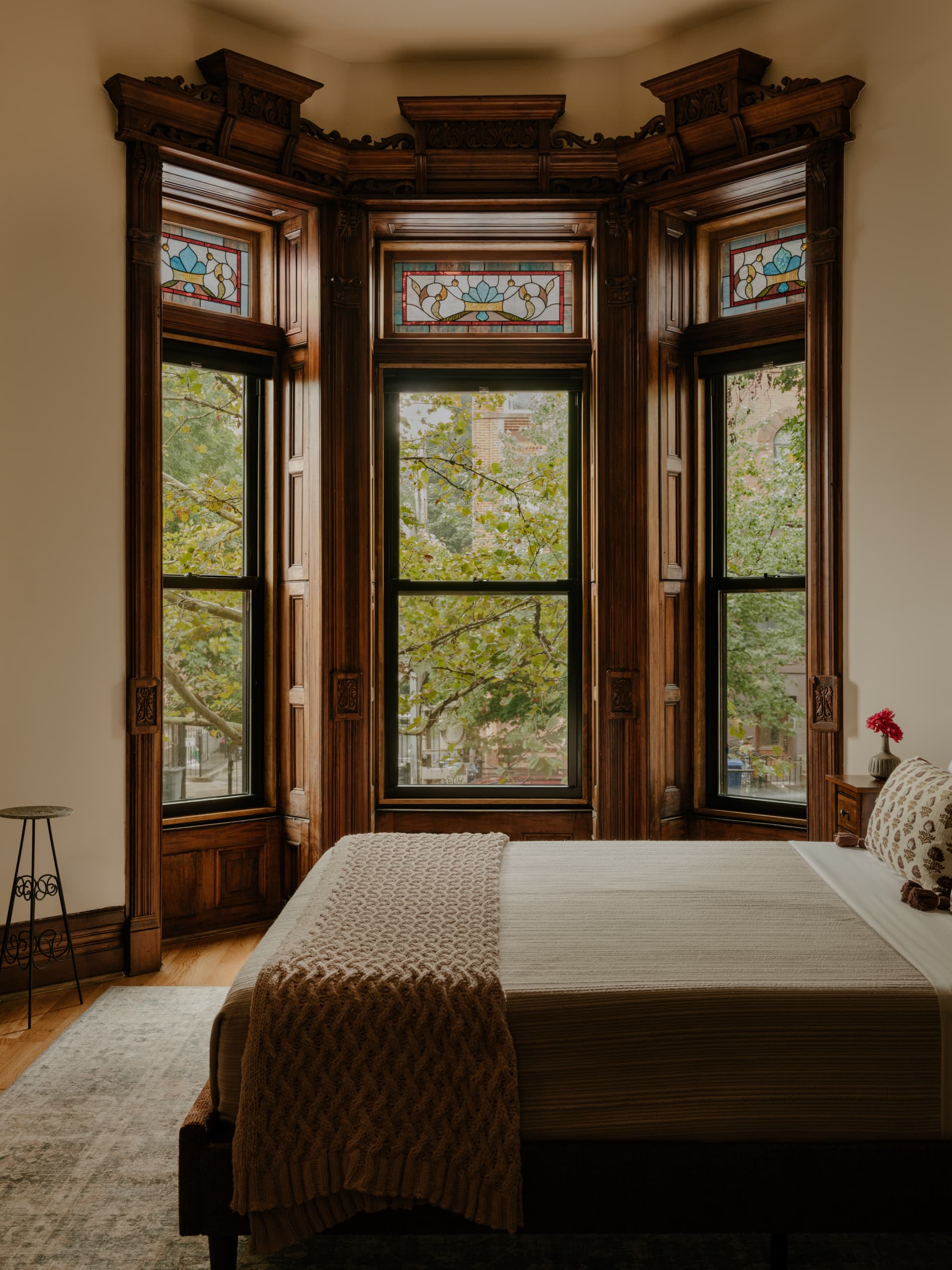A Halsey bedroom's bay window — carved wood, stained-glass transoms, the street's trees beyond
